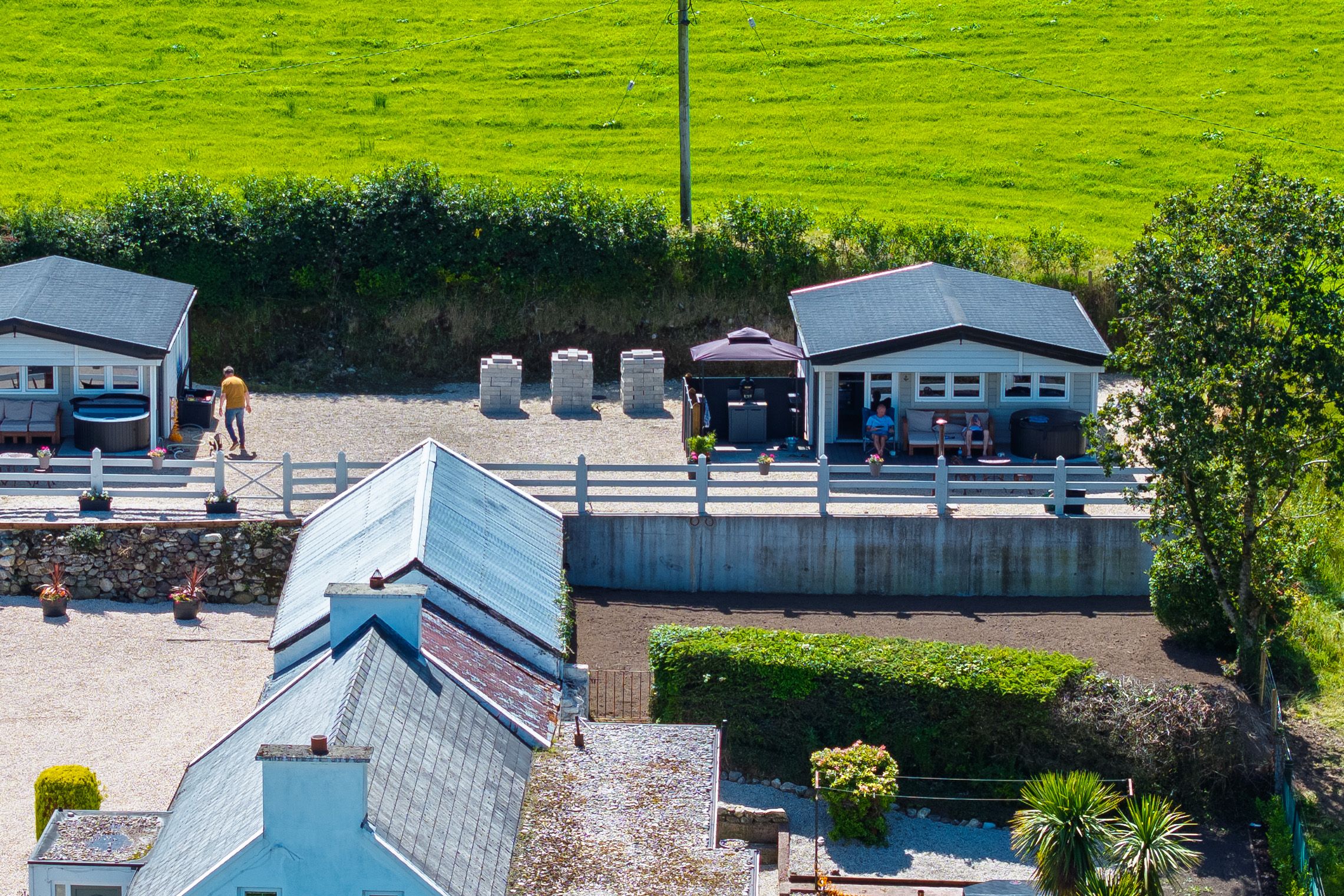 Aerial of the cottage below and the two log cabins on the terrace above, each with its own hot tub