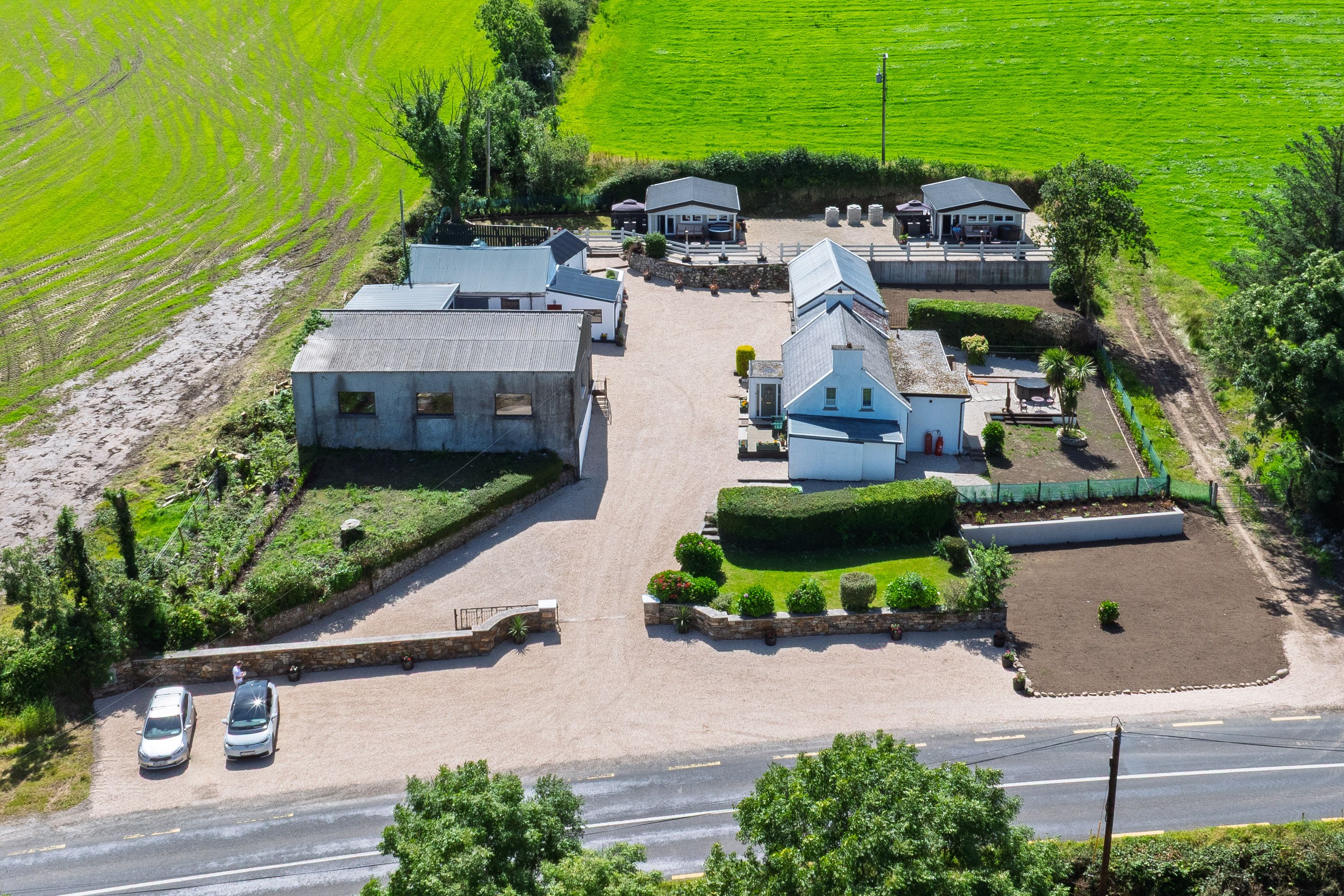 Overhead view of the site: cottage and outbuildings at road level, two cabins on the terrace behind
