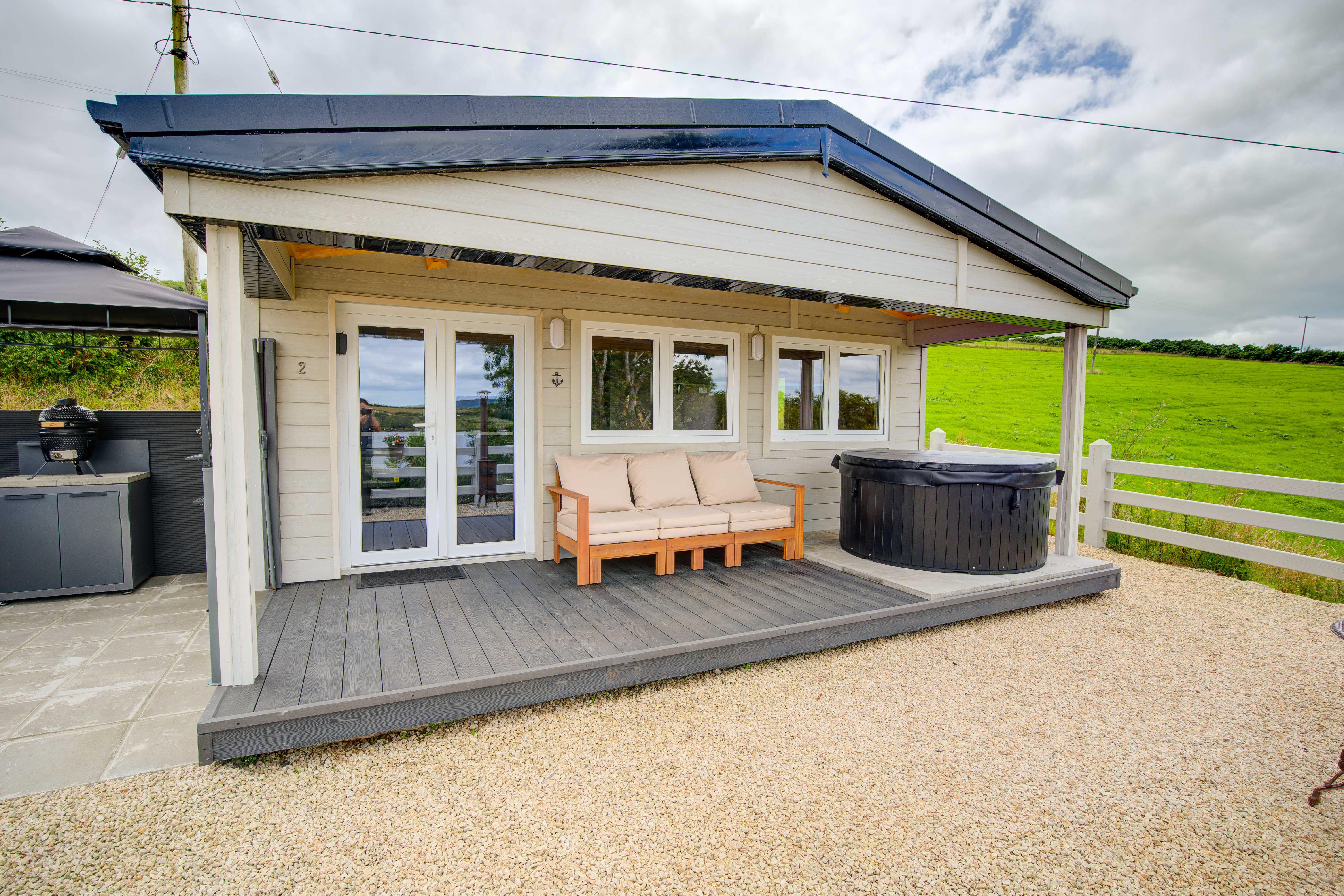 Cabin Two from the side path in daylight: pale grey weatherboard, pitched roof and veranda
