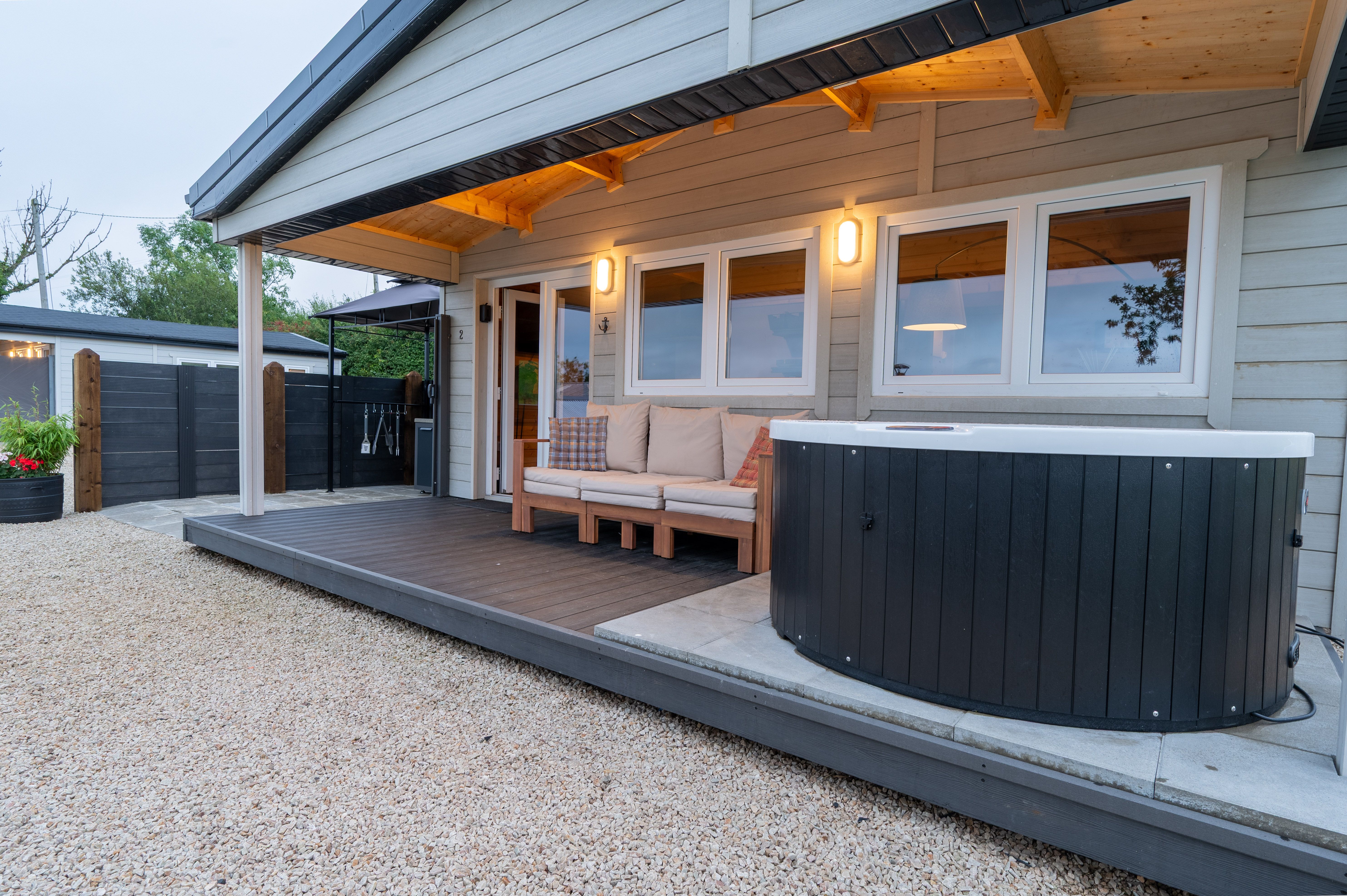 Cabin Two's covered deck at dusk, the hot tub beside the door with its '2' plaque