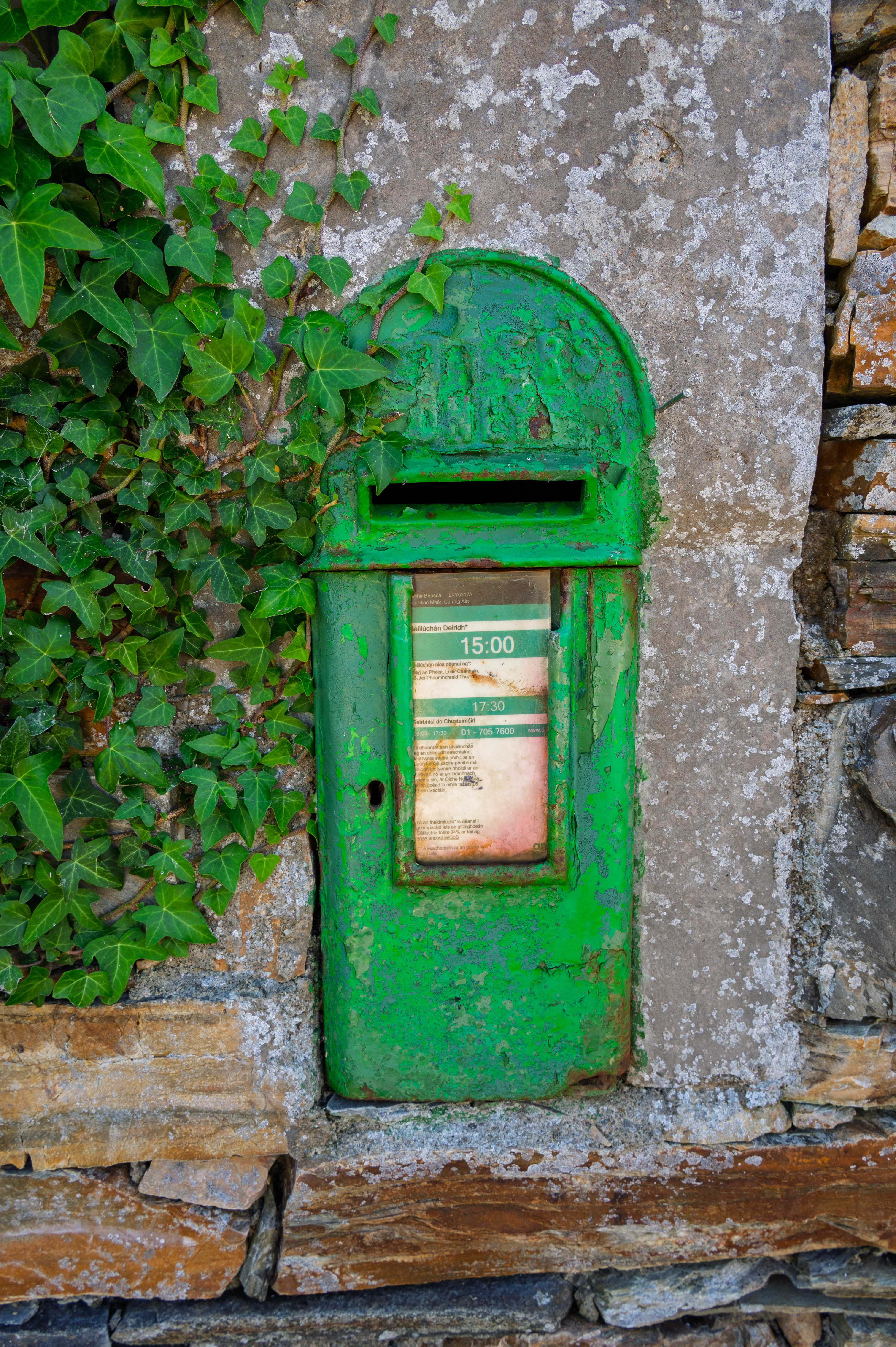 The old green An Post box set into a Carrigart stone wall, ivy alongside — letters and communication.