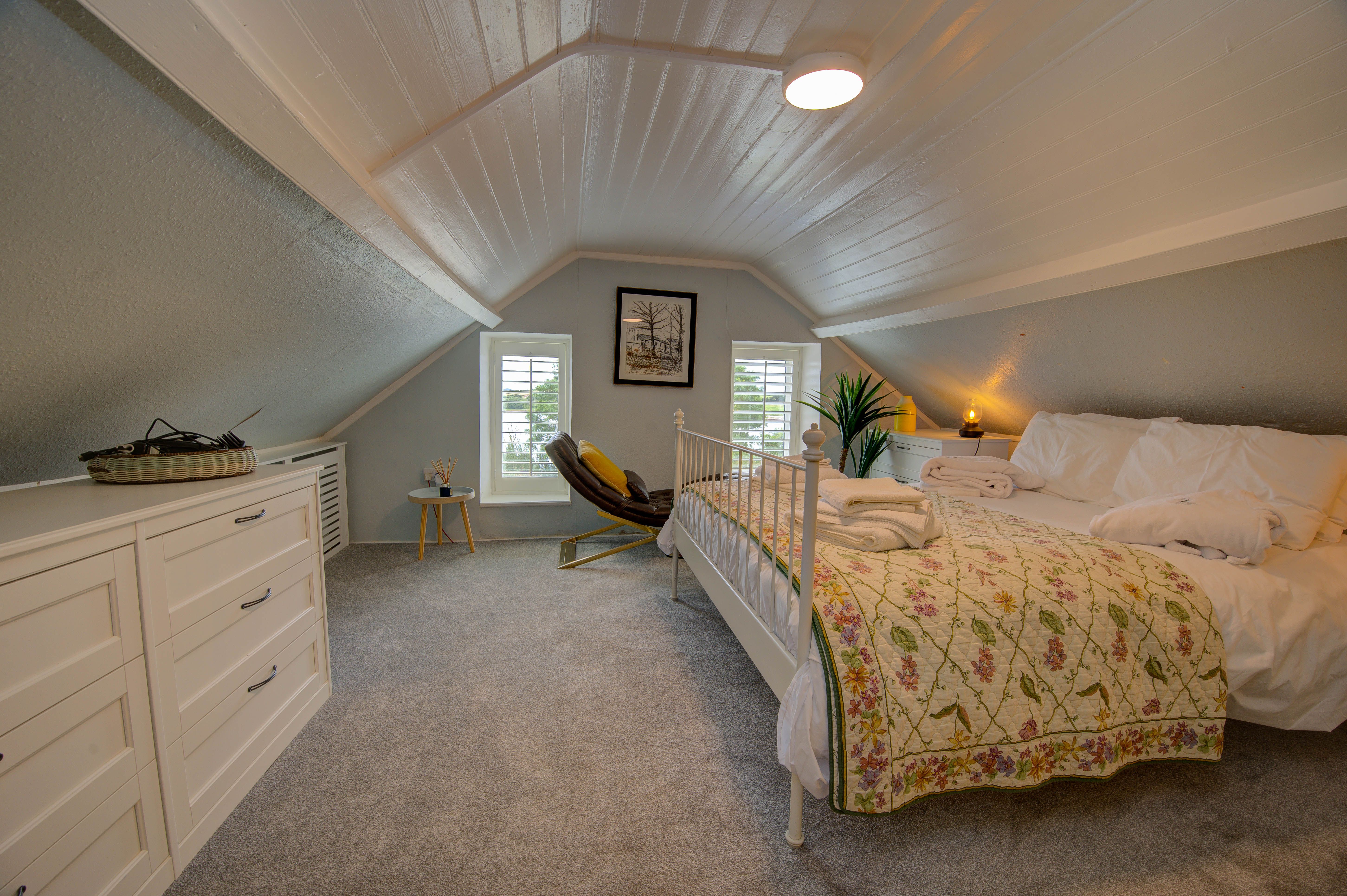 The cottage attic master bedroom: vaulted pine ceiling and a white wrought-iron double bed