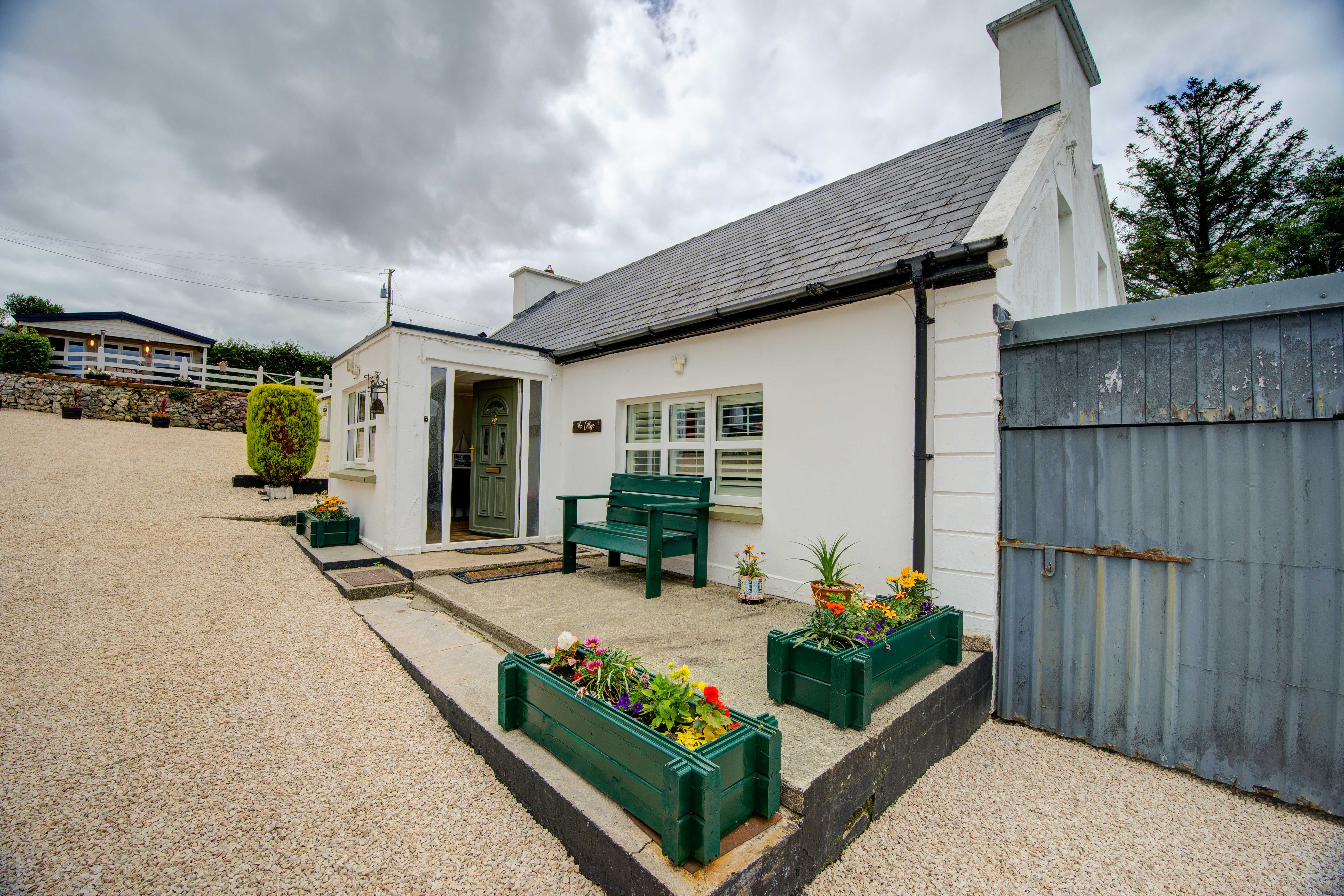 The cottage front from the gravel courtyard, with a cabin on the terrace above