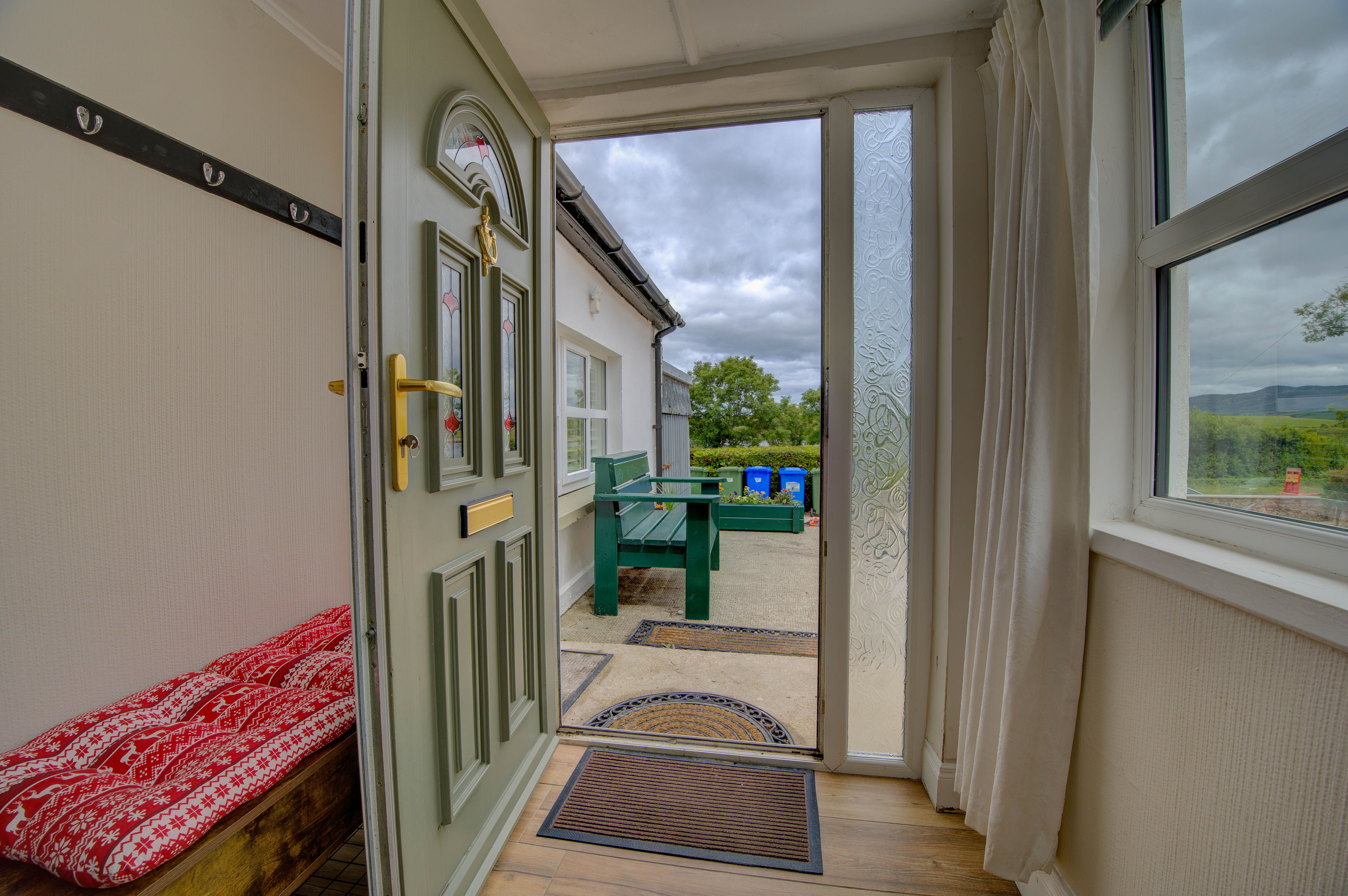 The cottage's open front door looking out to the gravel courtyard and the hills