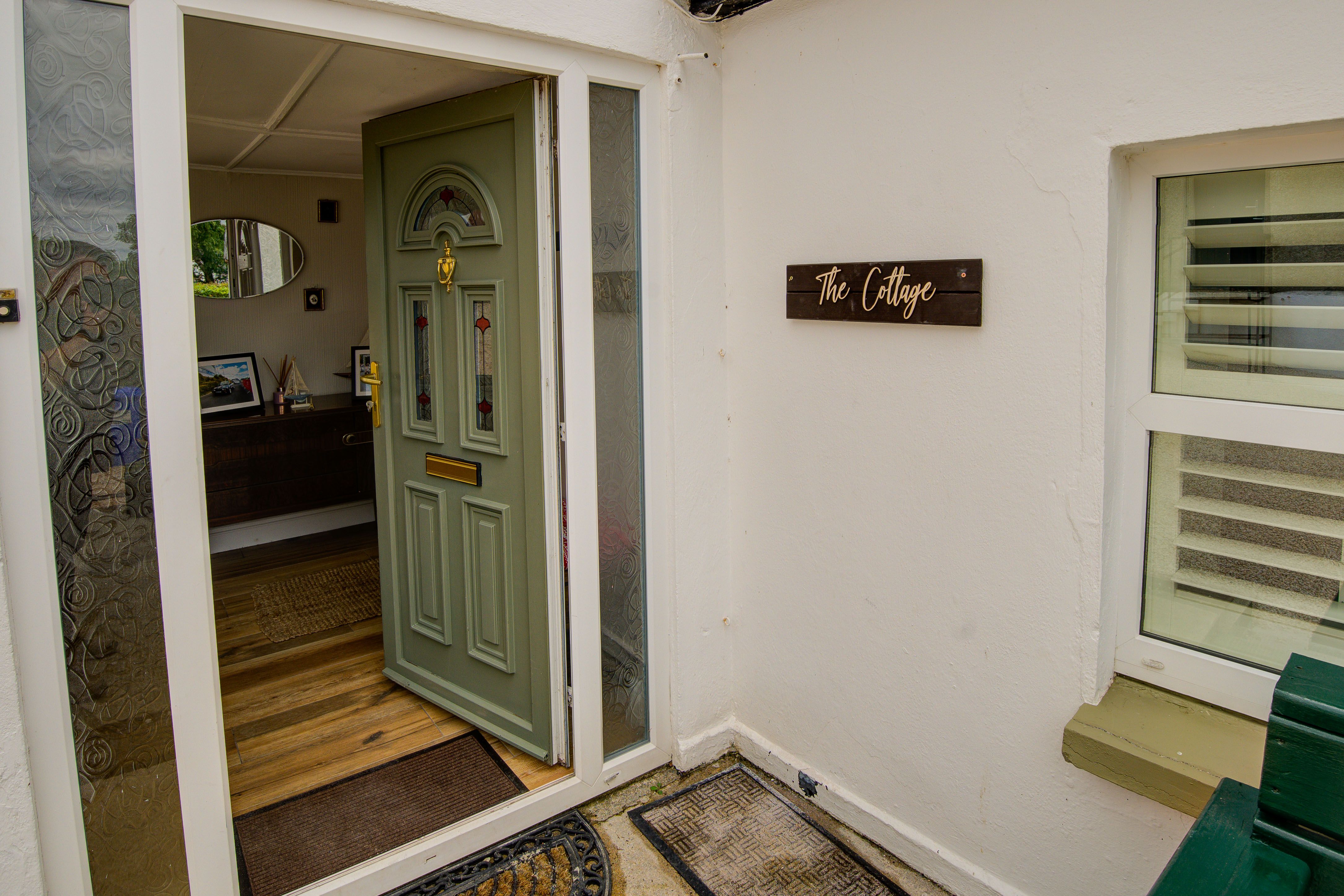 The cottage front entrance, the door open with “The Cottage” name plaque alongside.