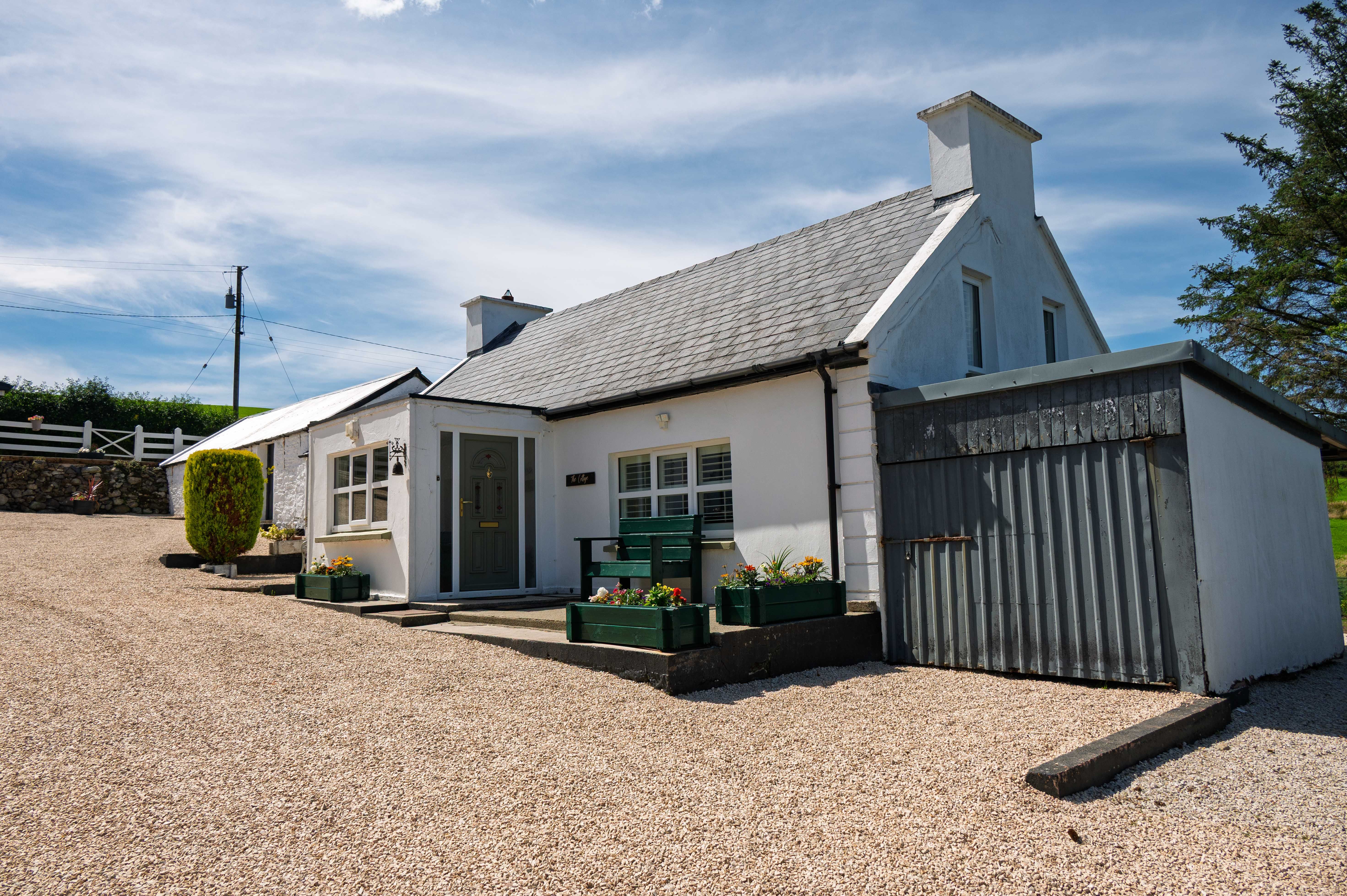 The finished cottage from the gravel courtyard — white render, slate roof and the red door.