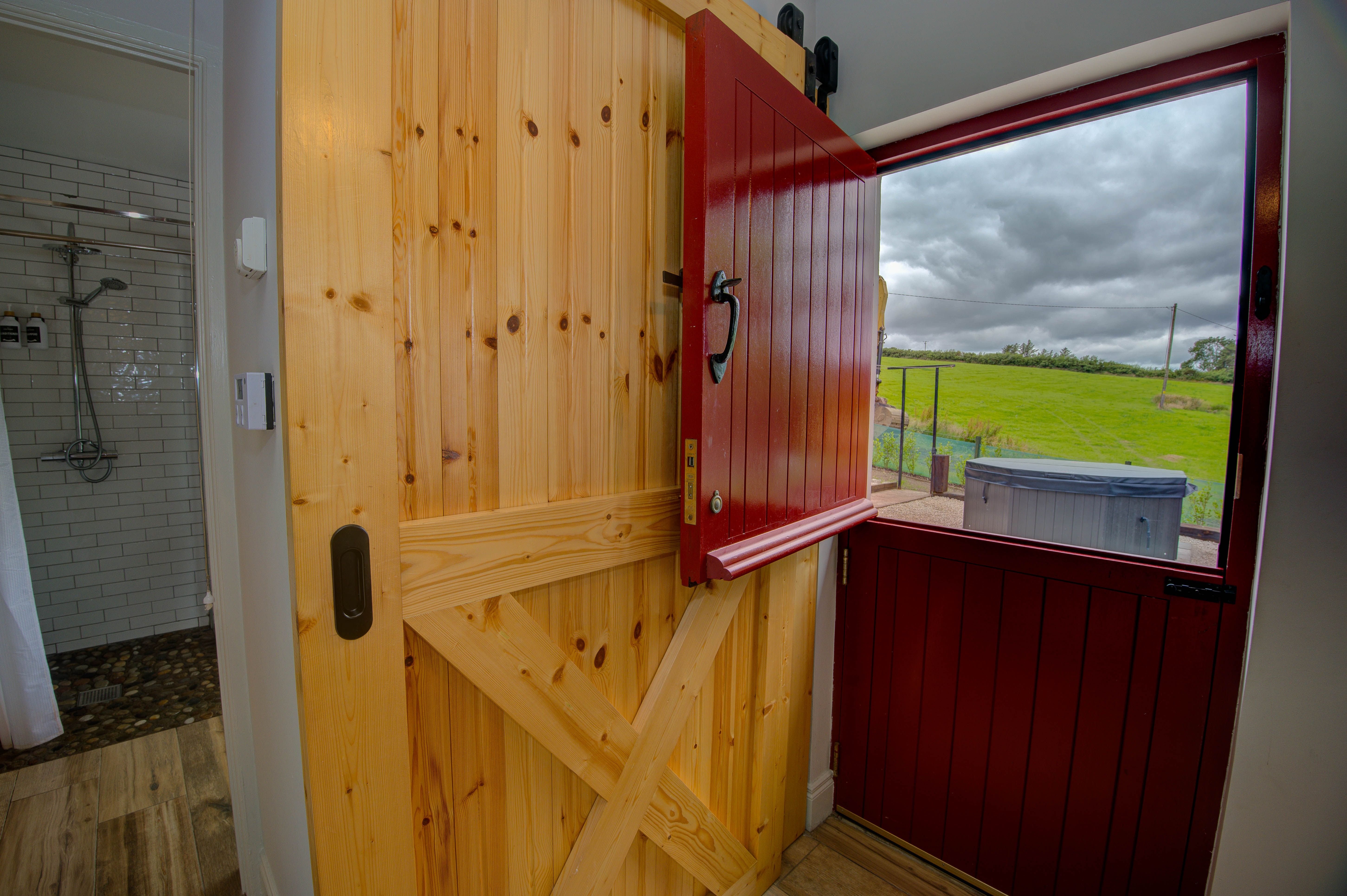 Inside the red Dutch door, the pine sliding inner door open onto the shower and the bay-view field beyond.