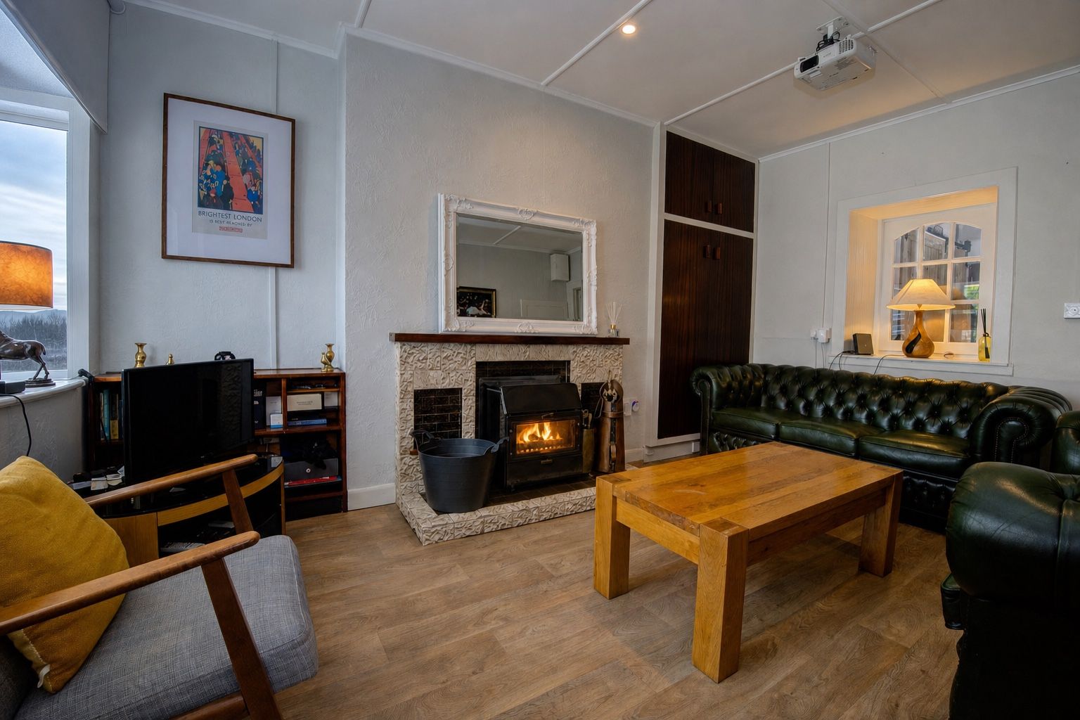 The cottage sitting room in winter, the cast-iron wood-burner lit in its white-tiled fireplace surround