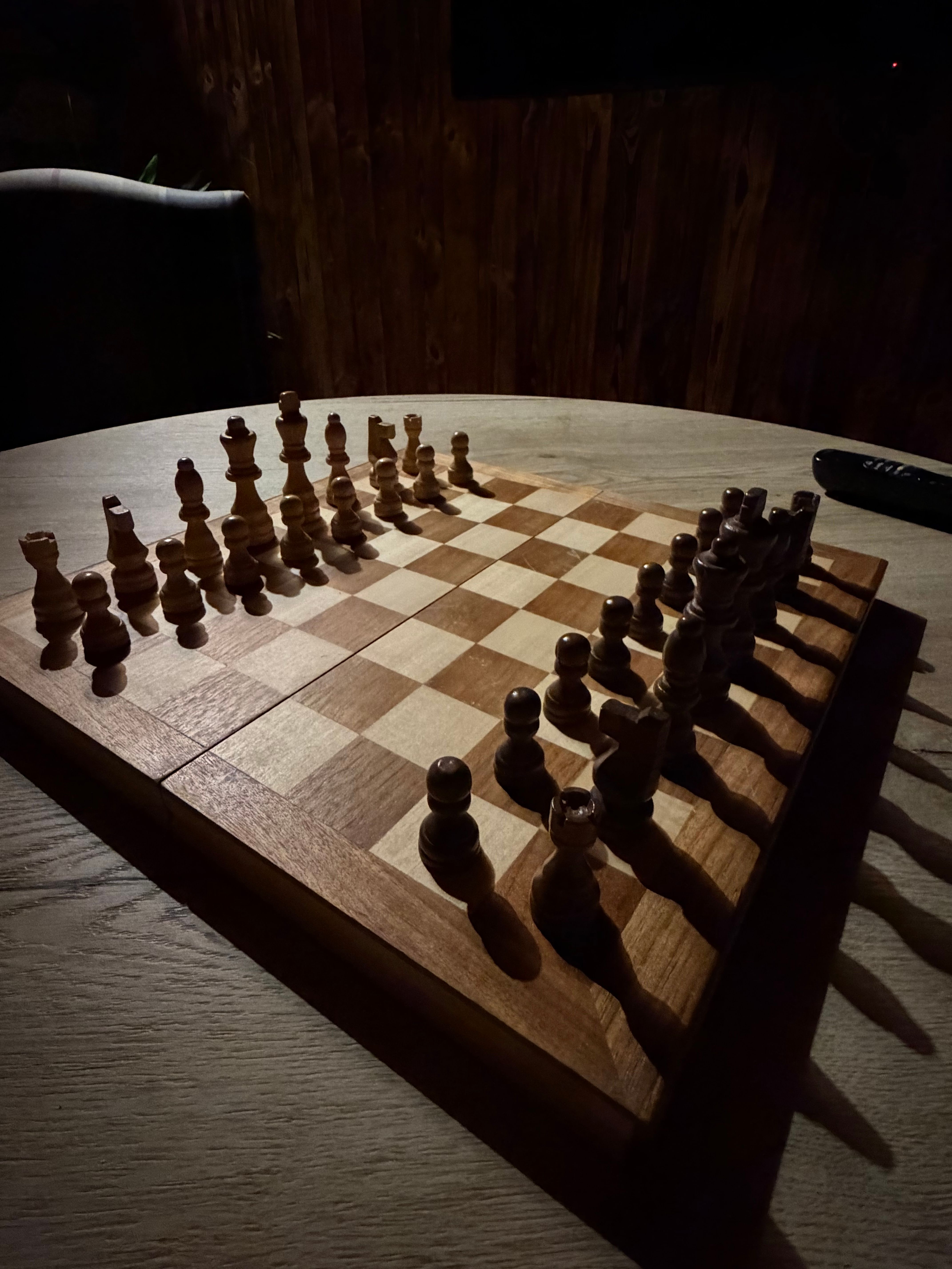 The games room chess board at a low, dramatic angle, white pieces in the foreground