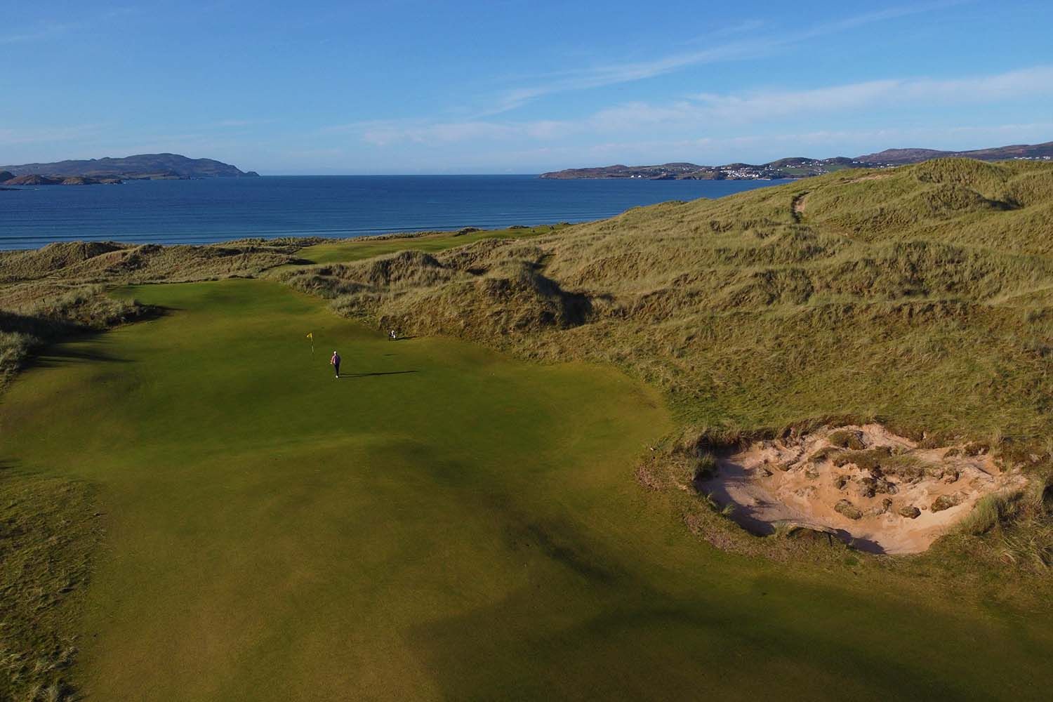 A golfer on a St Patrick's Links green in golden light, Sheephaven Bay behind