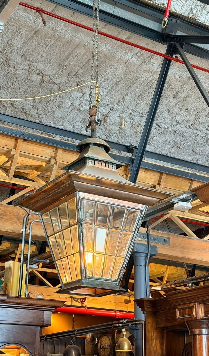 A large copper and leaded-glass lantern hanging from steel and timber trusses above the dark wood bar.