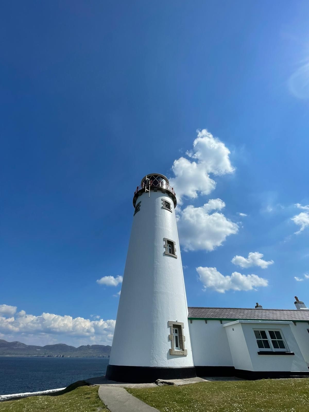 Looking up the white Fanad tower with its dark lantern gallery and red rail against a deep blue sky with bright cumulus clouds building behind