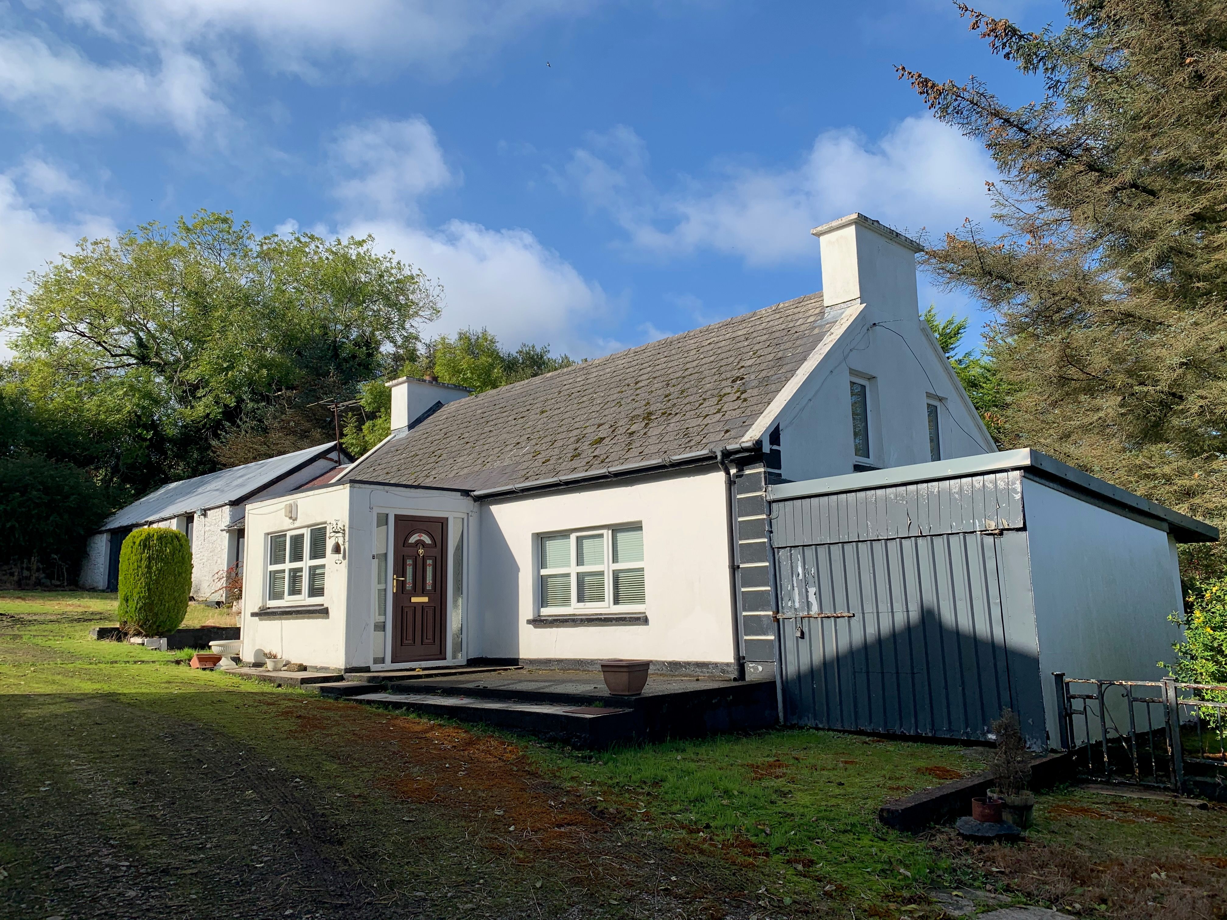 The cottage front before the work — tired grey render, a mossy slate roof and the red door, much as it had been left.