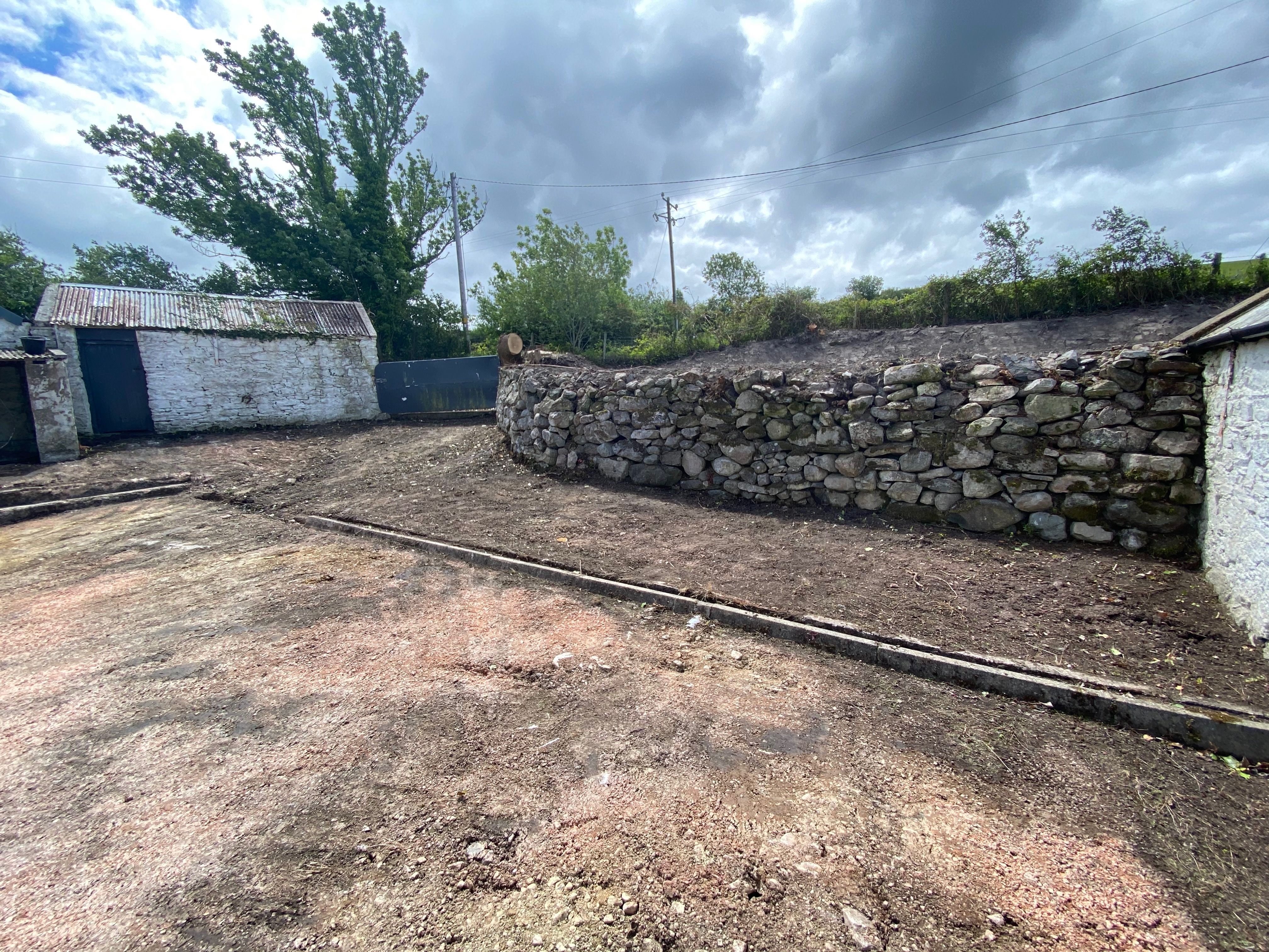 The old drystone wall curving along the edge of the yard, uncovered during the works after years under overgrowth.