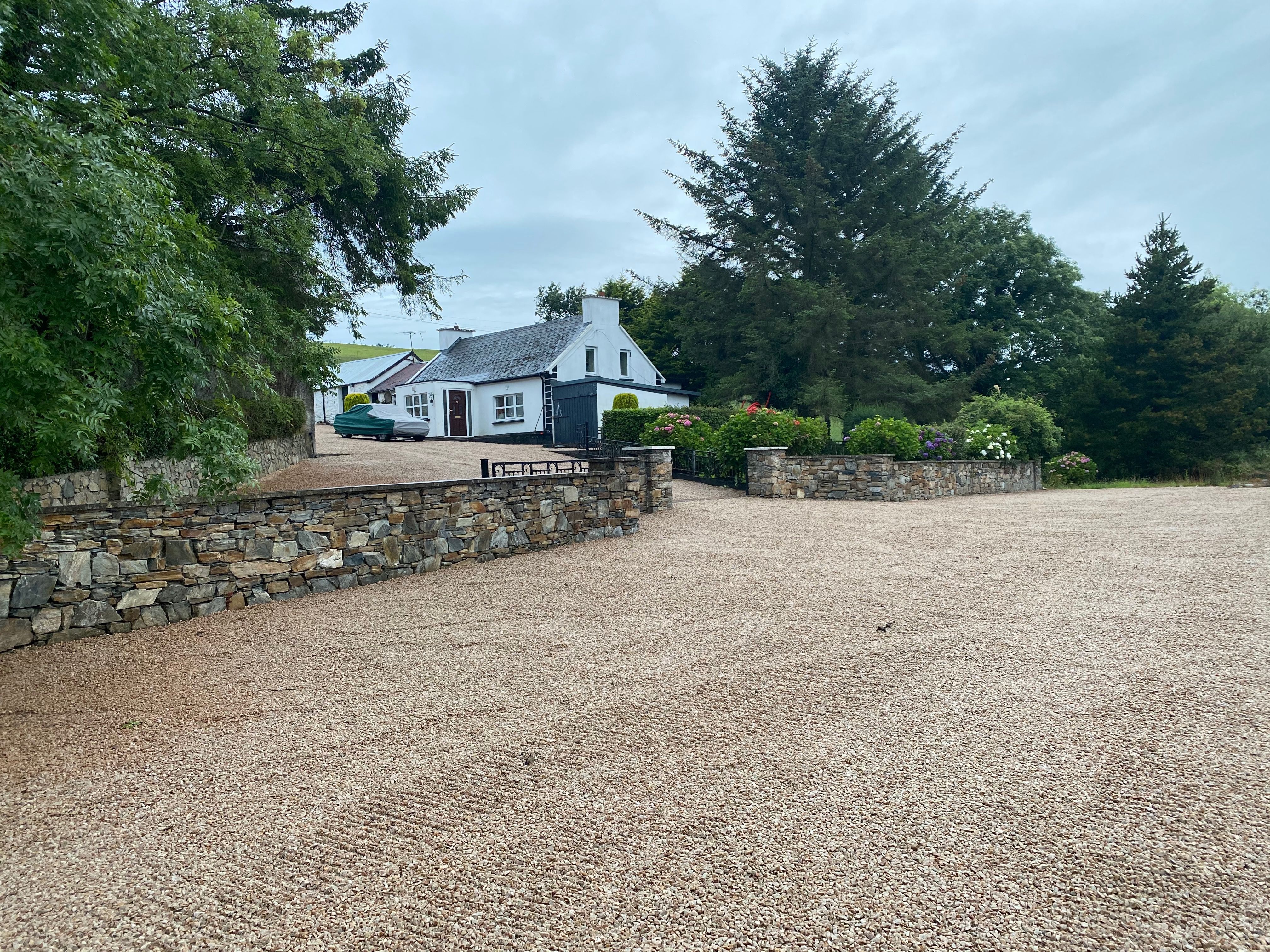 The finished property from the main-road end, the drystone wall and gravel sweeping up the Street to the cottage among the trees.