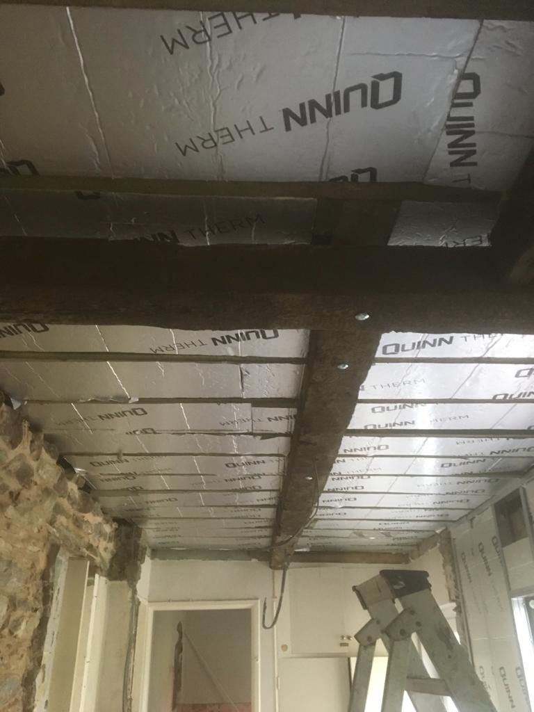 Insulation and reclaimed timber going into the roof, a heavy retained beam strapped across, the original stone wall to one side.