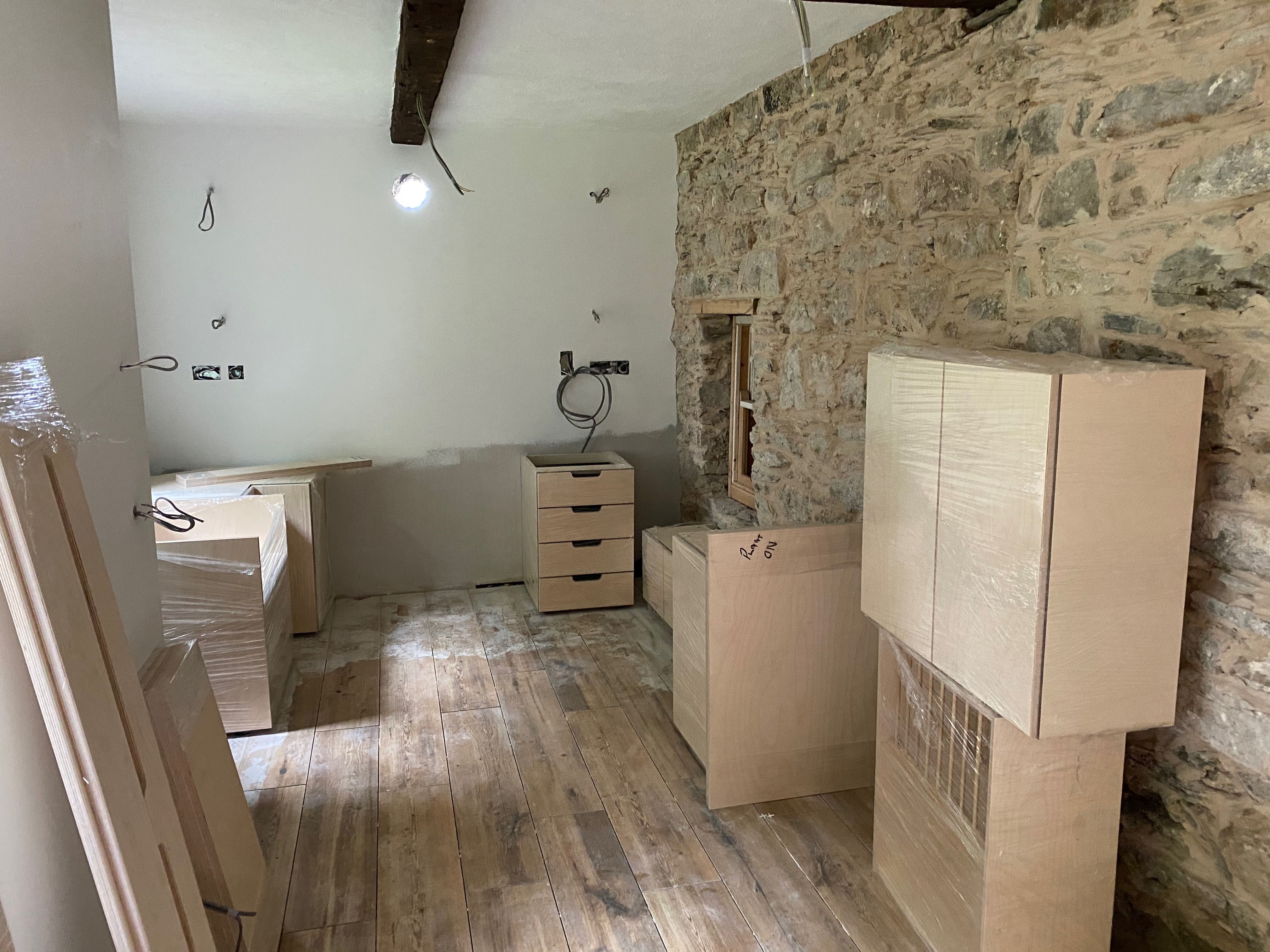 The new birch-ply kitchen units arriving on site against the exposed stone wall, the deep window reveal newly framed in timber.