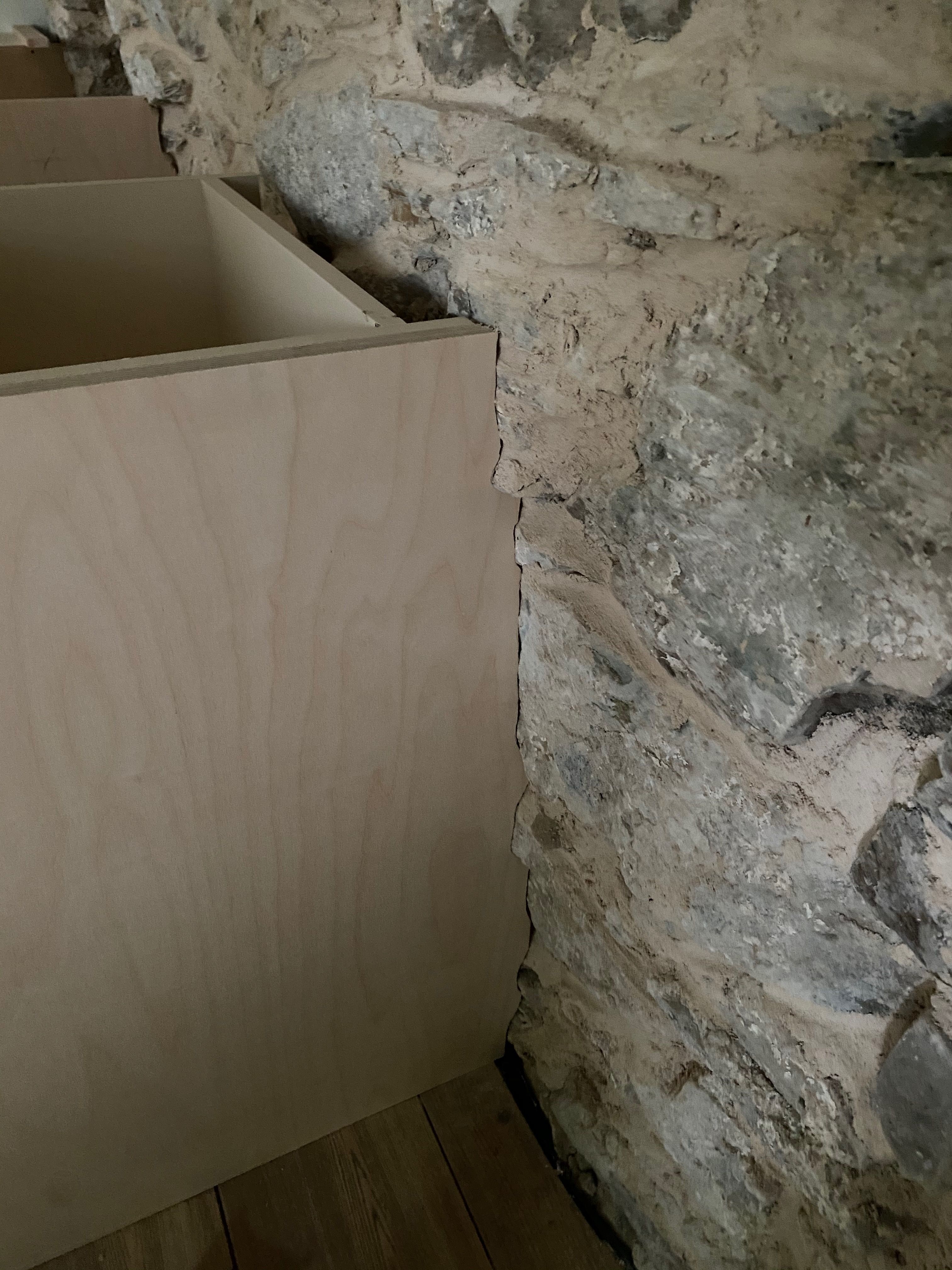 Detail of the new countertop scribed tight against the rough exposed stone wall, no gap between straight slab and uneven stone.