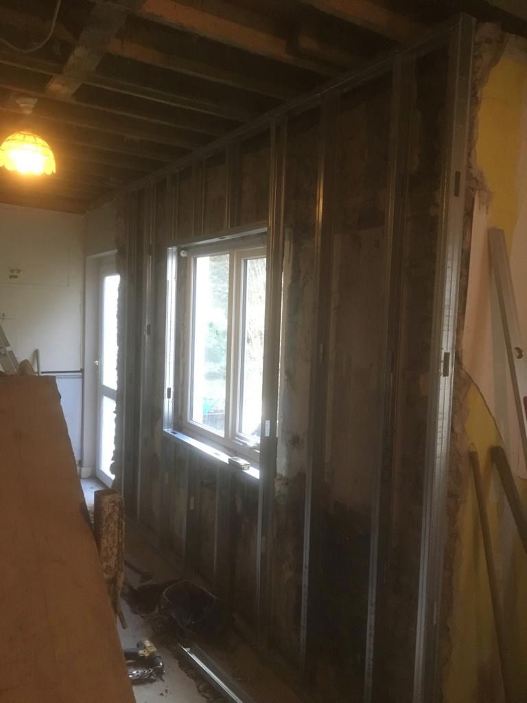 New galvanised metal studwork going up to dry-line the kitchen, the stone wall and stripped ceiling behind.