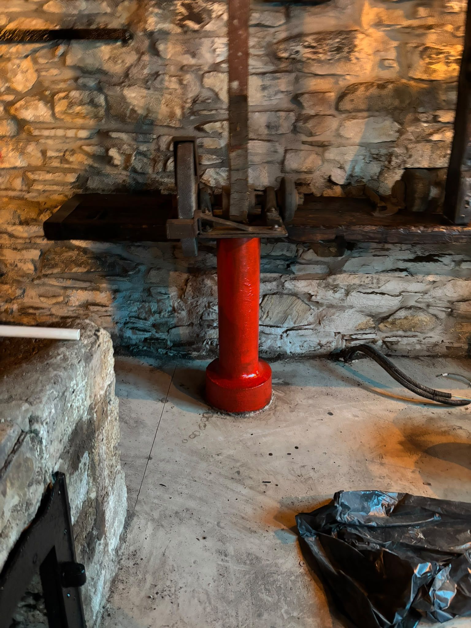 The old grinding wheel and its bench on a freshly painted red cast-iron pedestal against the stone wall, the old stone trough with a new black door at the left.