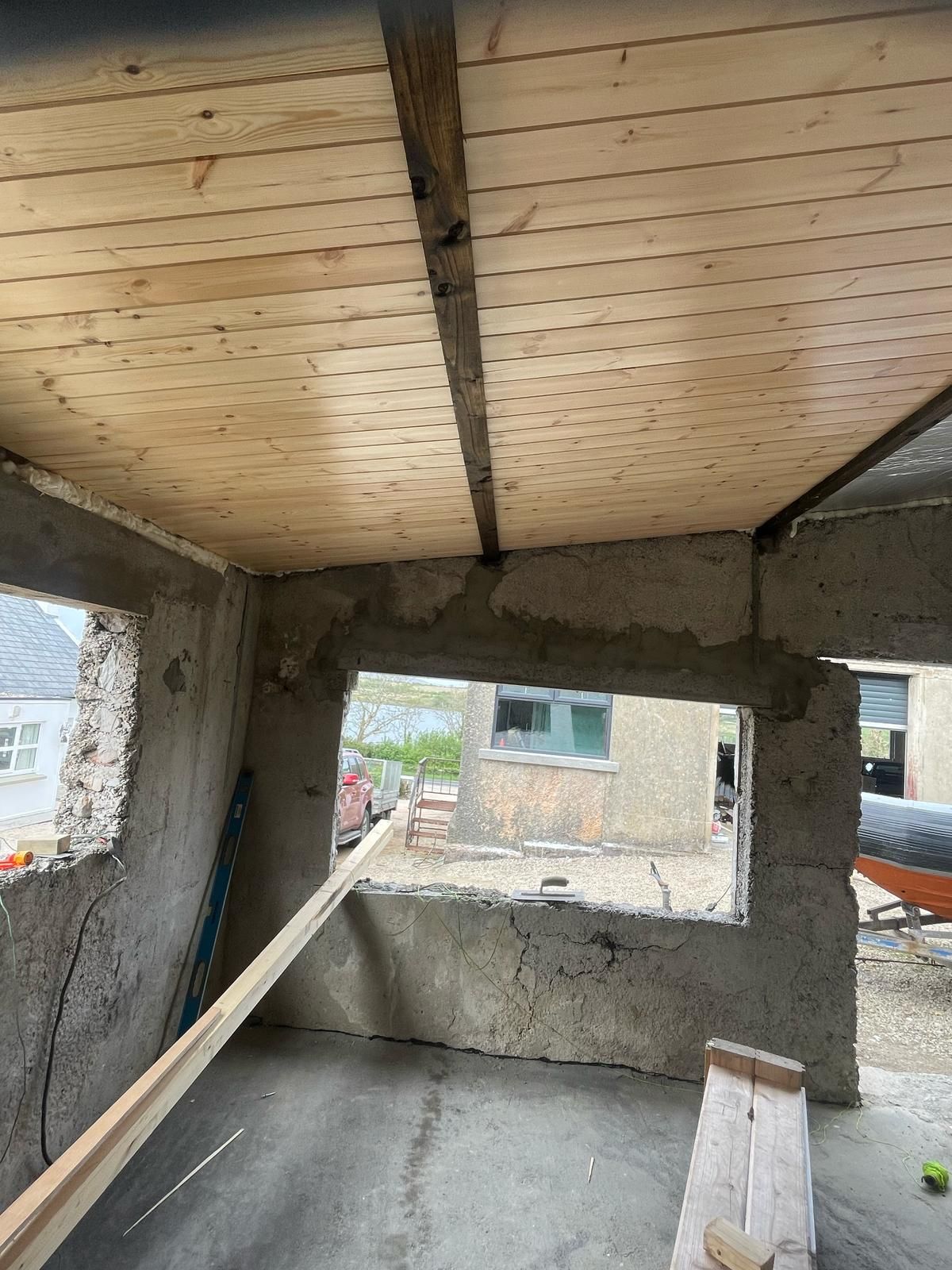 The games-room interior with the pale-pine tongue-and-groove ceiling installed and a dark beam across the centre, walls still bare concrete.