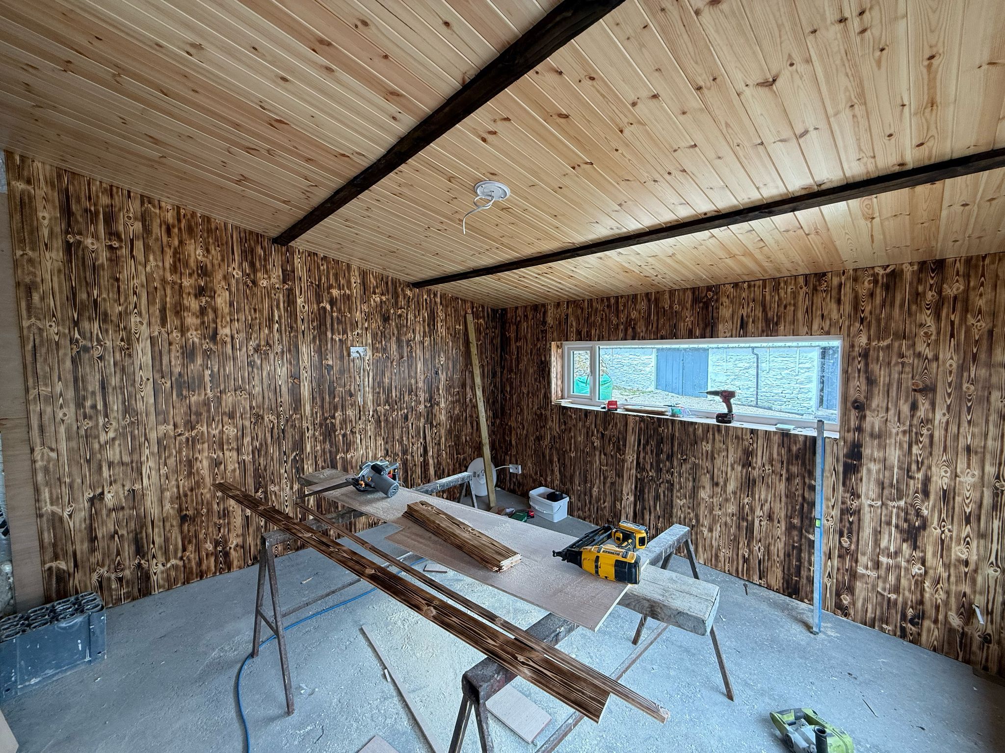Vertical burnt-pine tongue-and-groove cladding going up on the games-room walls, the pale ceiling and dark beam above.