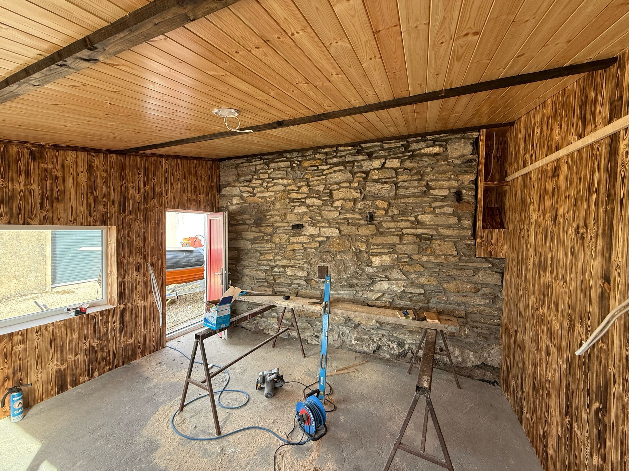 The dry-stone feature wall at the back of the games room, preserved and freshly pointed, framed by charred-pine cladding under the pale-pine ceiling.