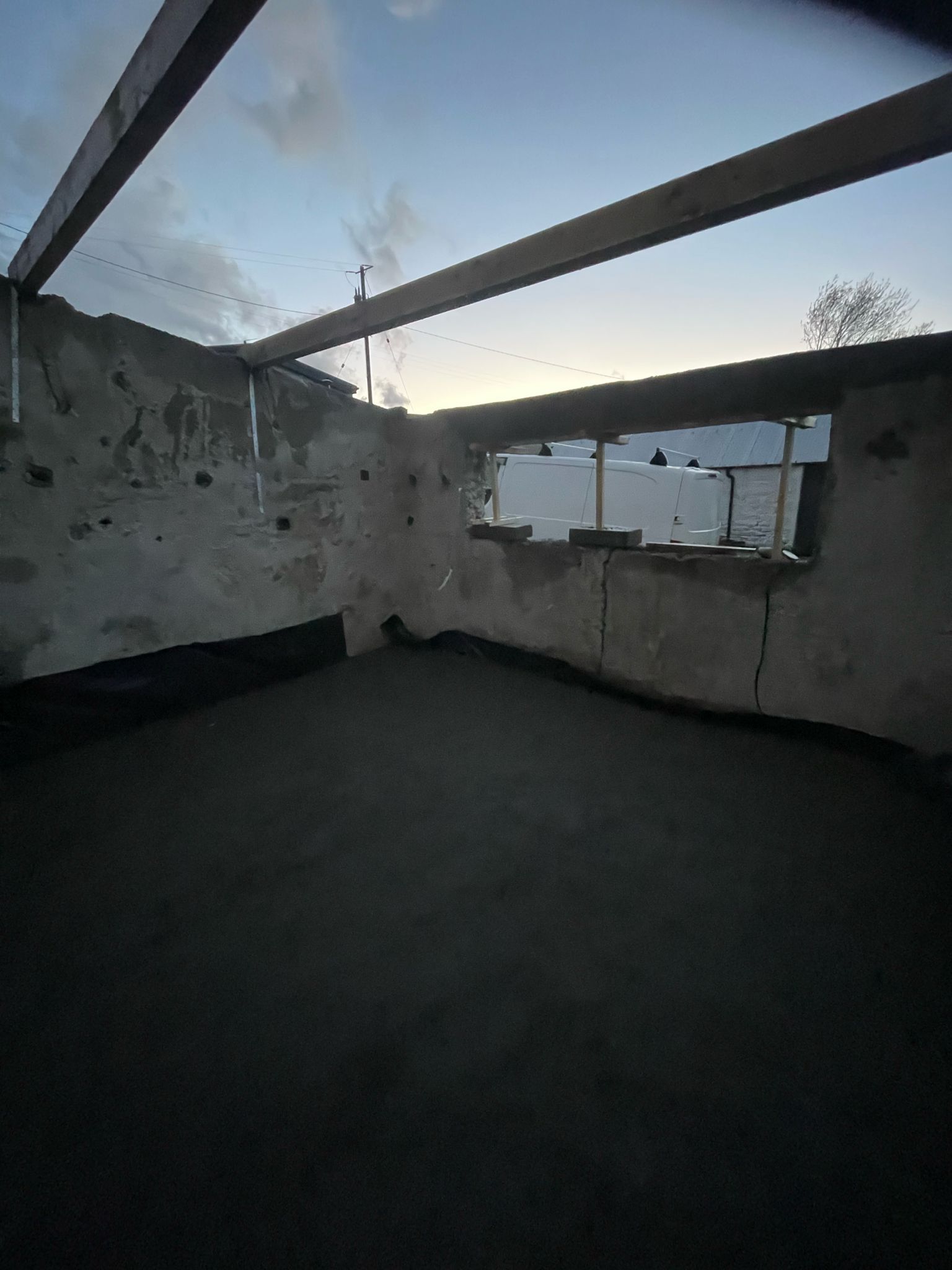 The forge with its roof off at dusk — bare timber rafters across the wall-tops, the bay-side wall opened up, before the games room went in.