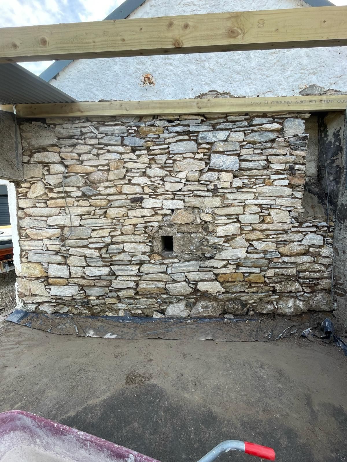 Close-up of the dry-stone forge gable, original stonework with a small vent opening and a fresh timber wall-plate above.