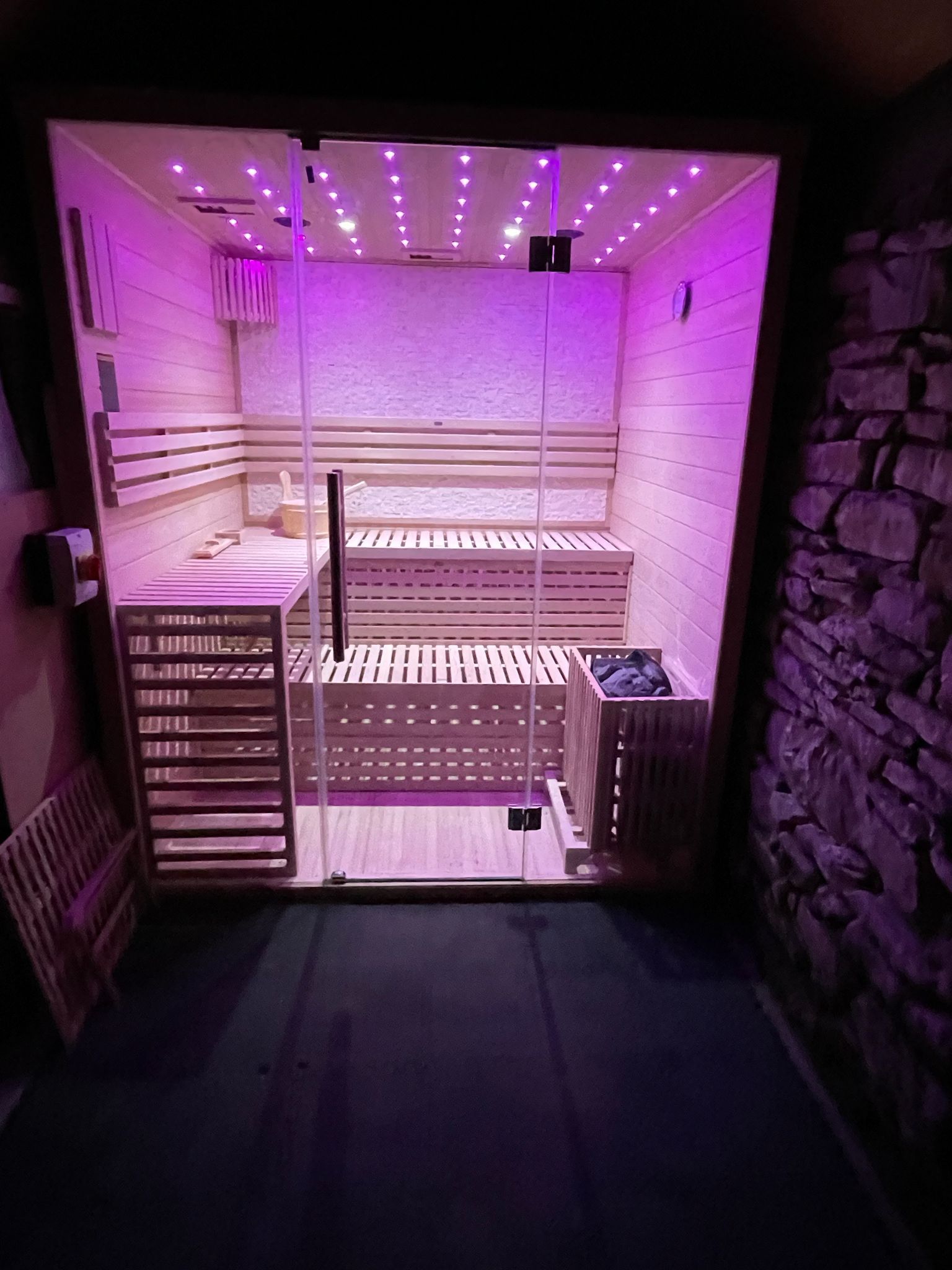 Looking through the glass cabin door into the lit sauna — pine-slat benches, the heater with its stones, the lights on for the first time.