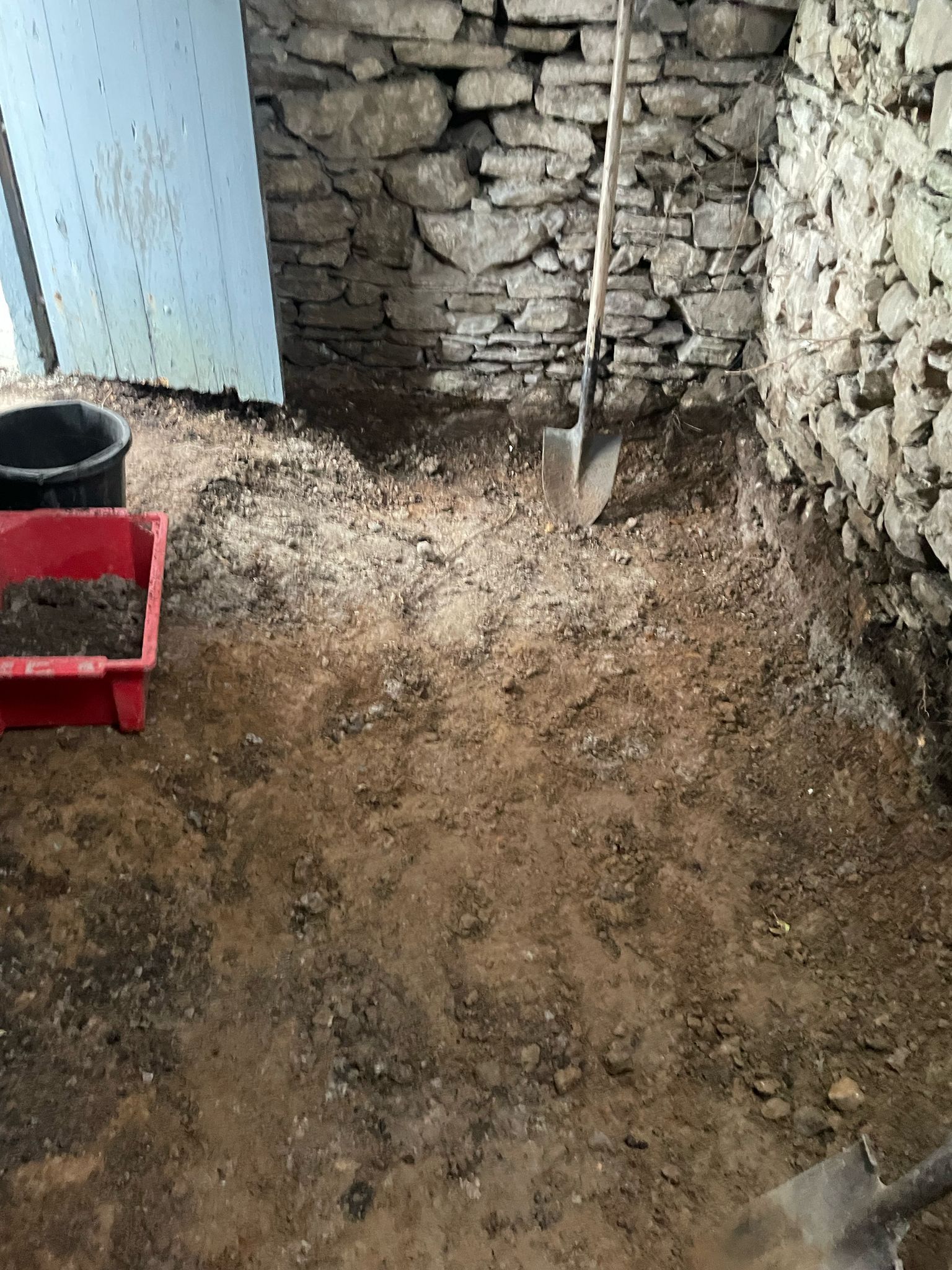 The peat shed interior stripped back — floor dug to bare earth, a spade standing in the dirt, dry-stone walls exposed.