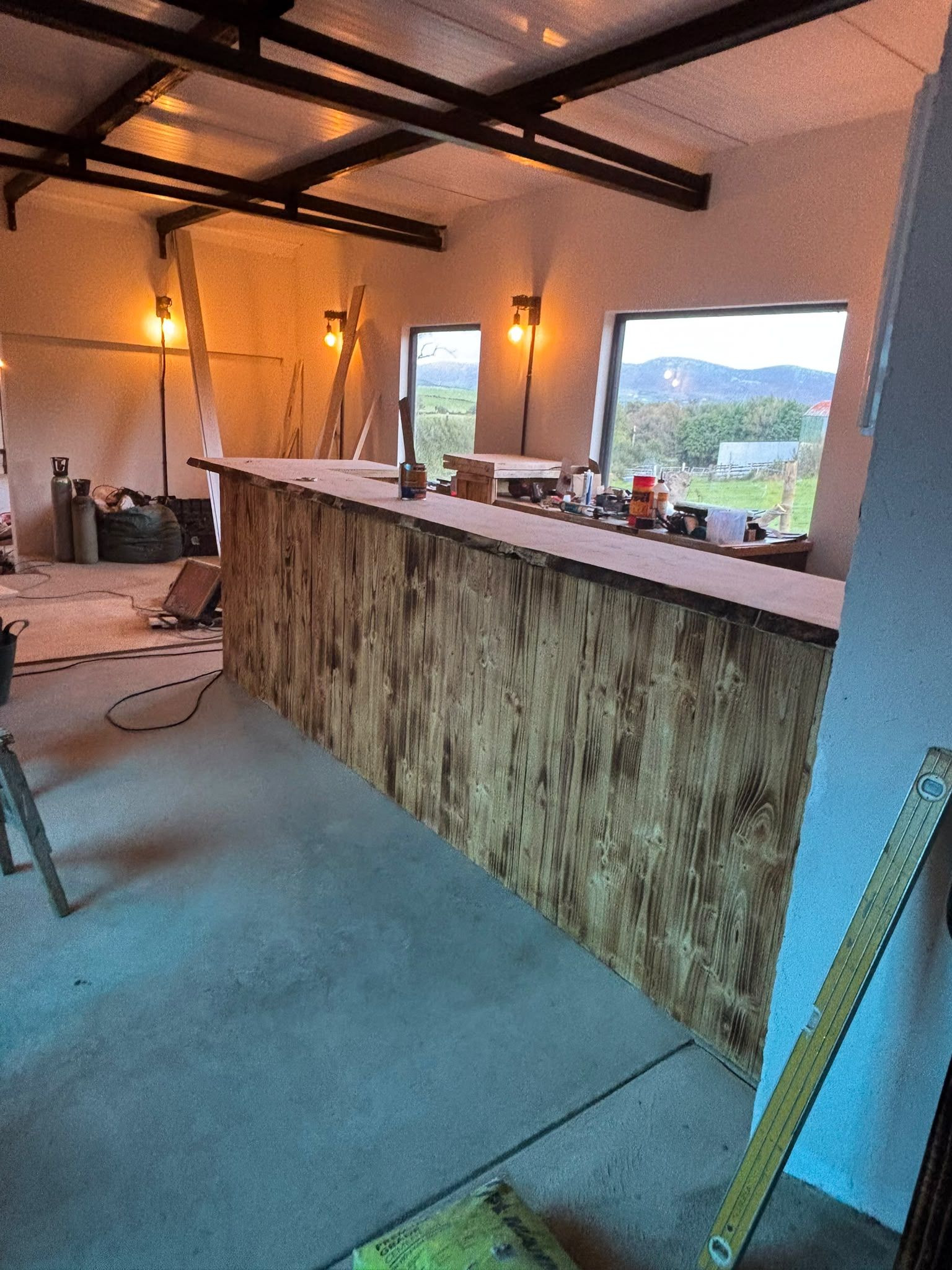The long scorched-timber bar under the black steel trusses of the workshop, two windows looking out to the hills.
