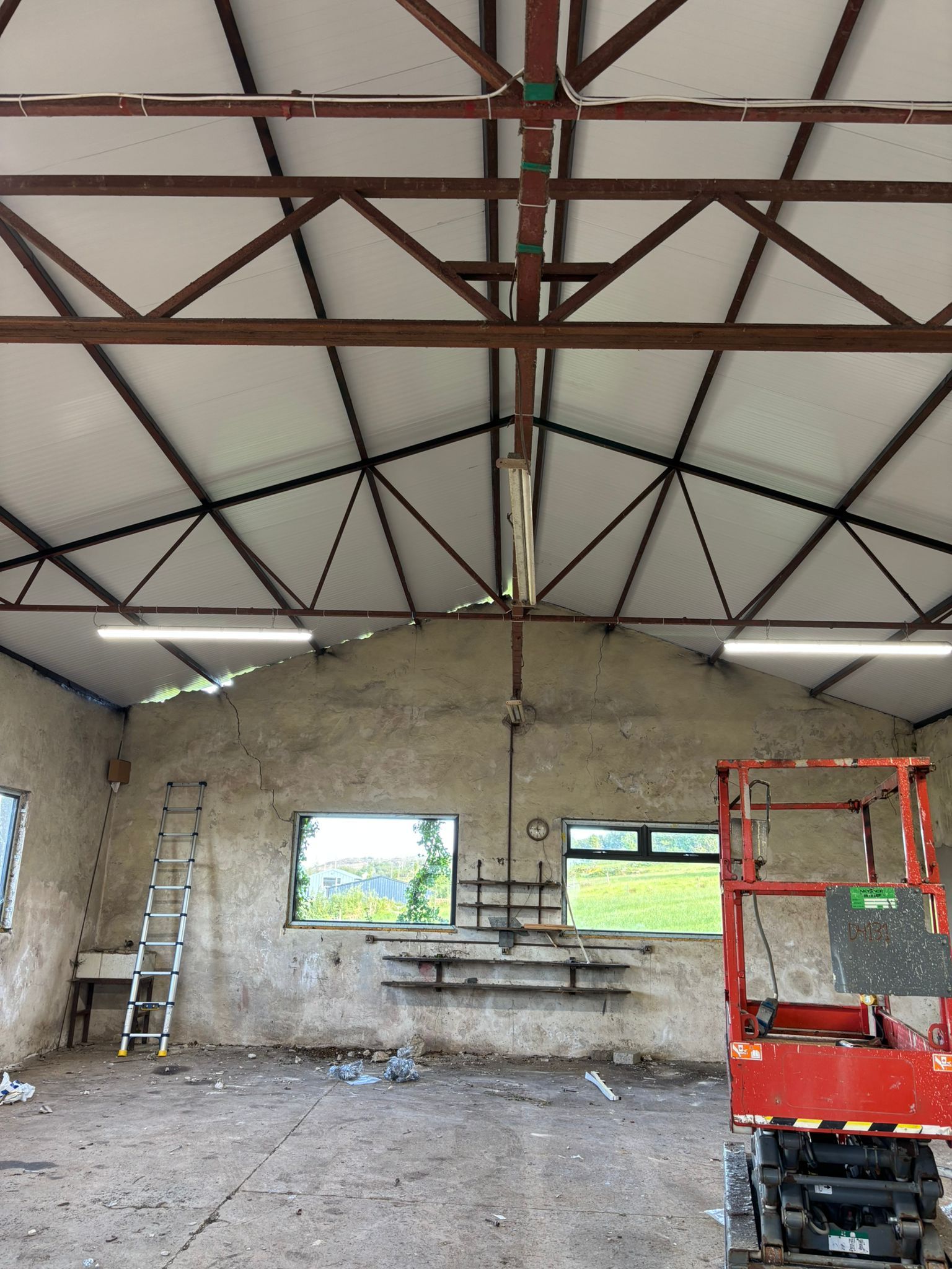 The workshop interior during re-roofing, the new white Kingspan insulated panels fixed under the steel trusses, the room dry and bright.