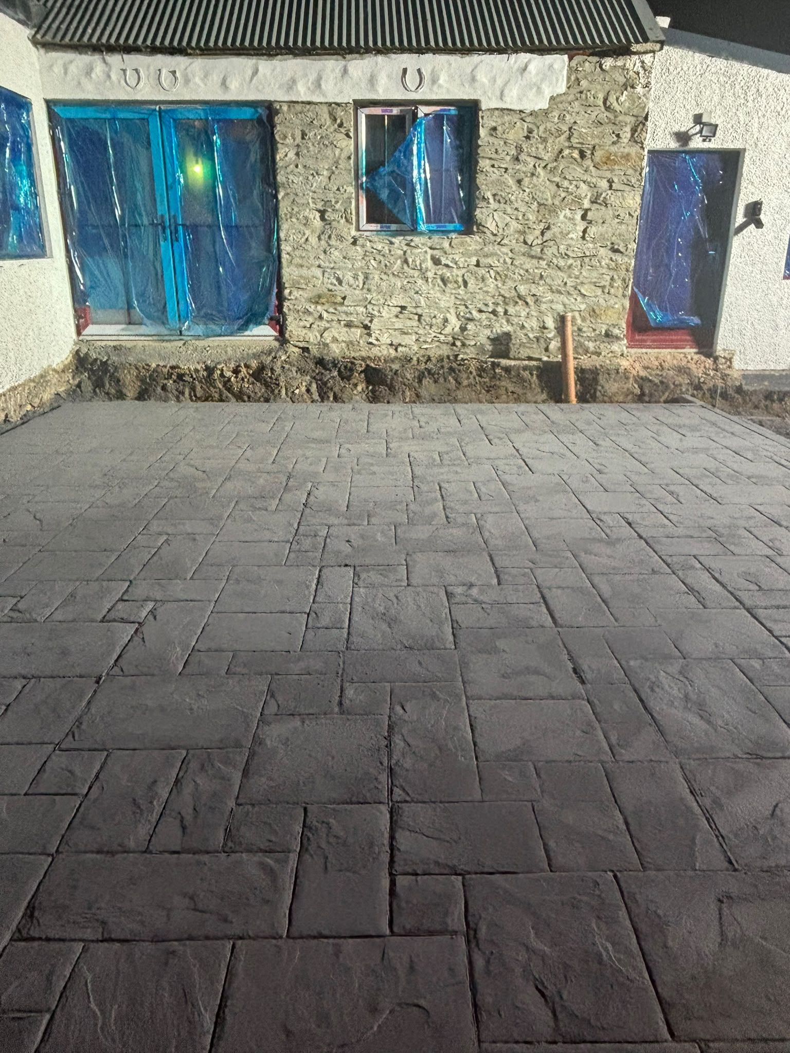 The new stamped-concrete yard in front of a stone wall with red-framed French doors and three horseshoes.
