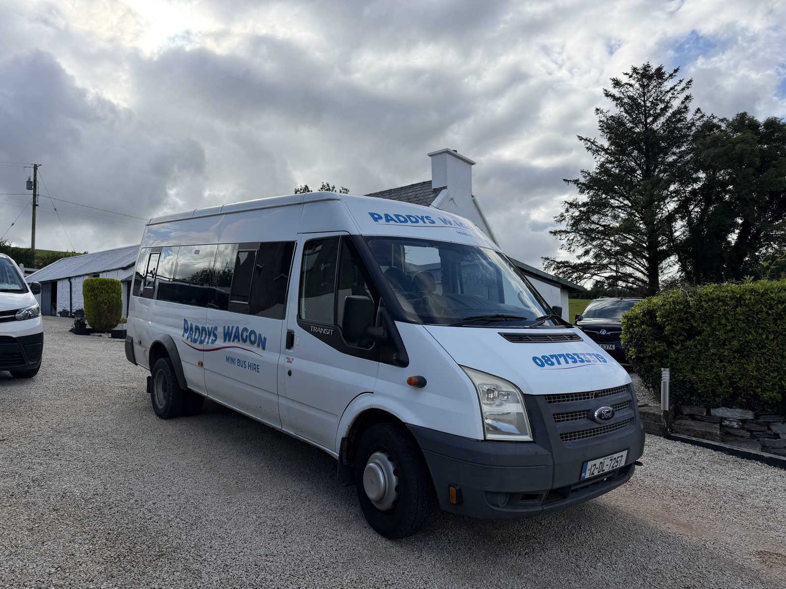 The Paddys Wagon minibus, a white long-wheelbase Ford Transit, parked on gravel outside a white cottage